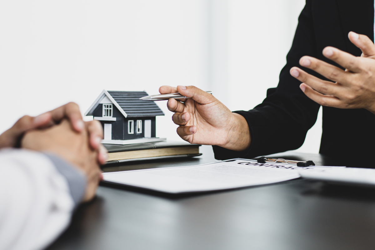 two people's hands over a desk with a model home and paperwork