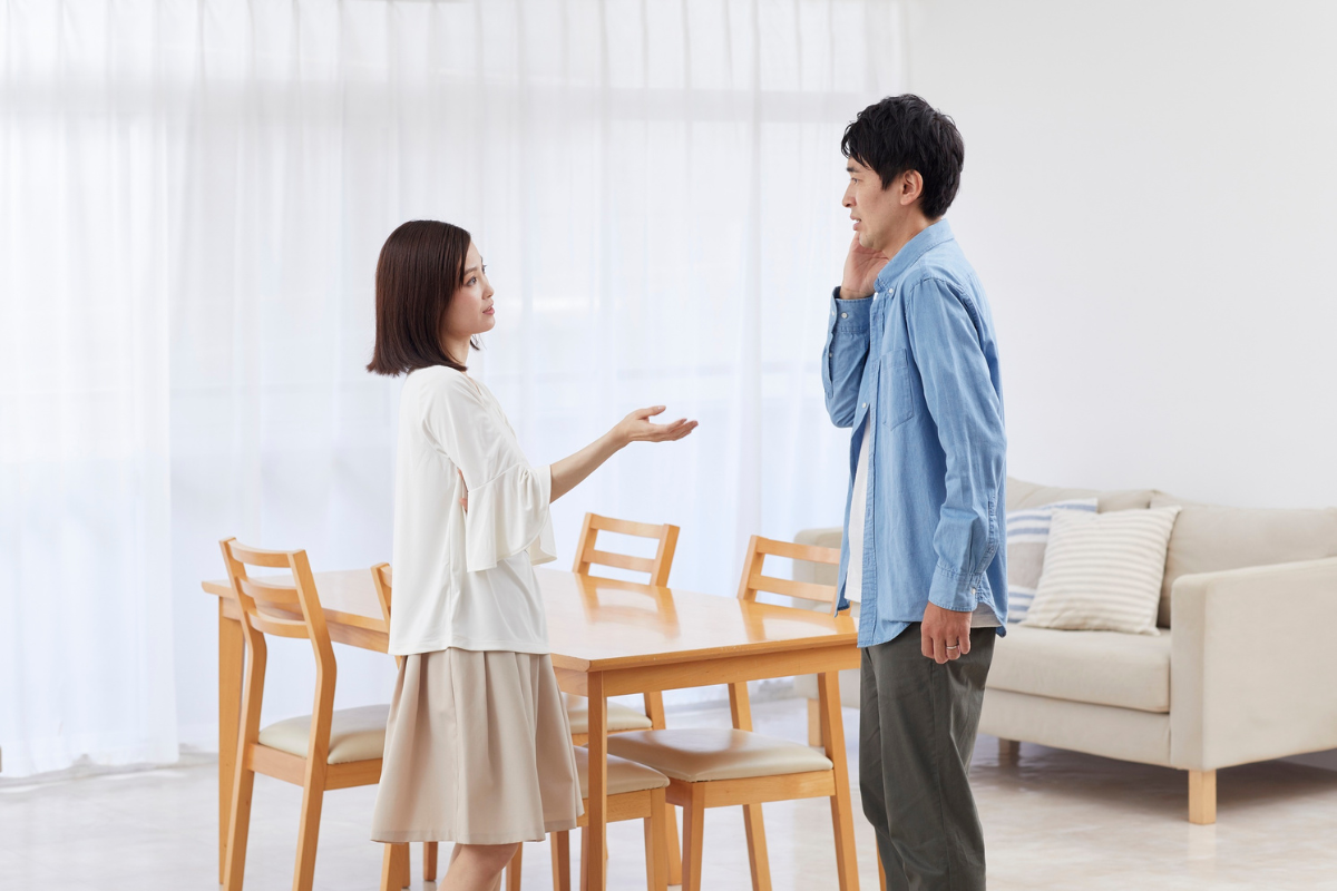 adult male and female standing in a living room in front of a dining table with expressions of misunderstanding