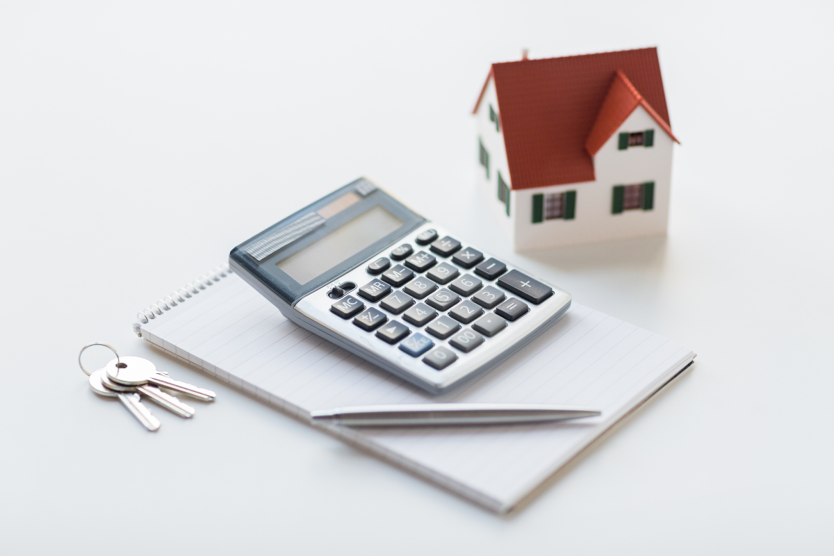 a model home miniature on a white desk with a calculator, pen, notepad, and keys